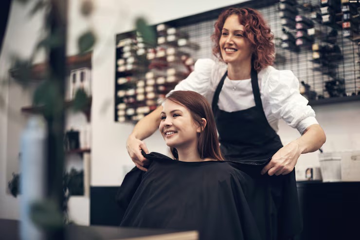 Smiling stylist removing the cape from a happy client after a service in one of the salon suites for rent in Marietta, the loyal relationship that steadies income during the slow season.