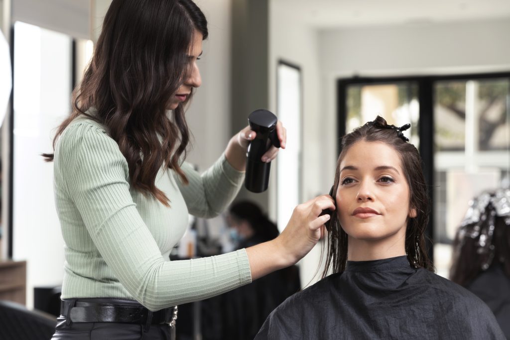 Stylist spritzing water on a calm client's hair during a service, showing the service and retail revenue possible with Sandy Springs salon suites for rent. Sandy Springs salon rental